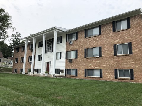 a large brick building with white siding and a large grassy area in front of it