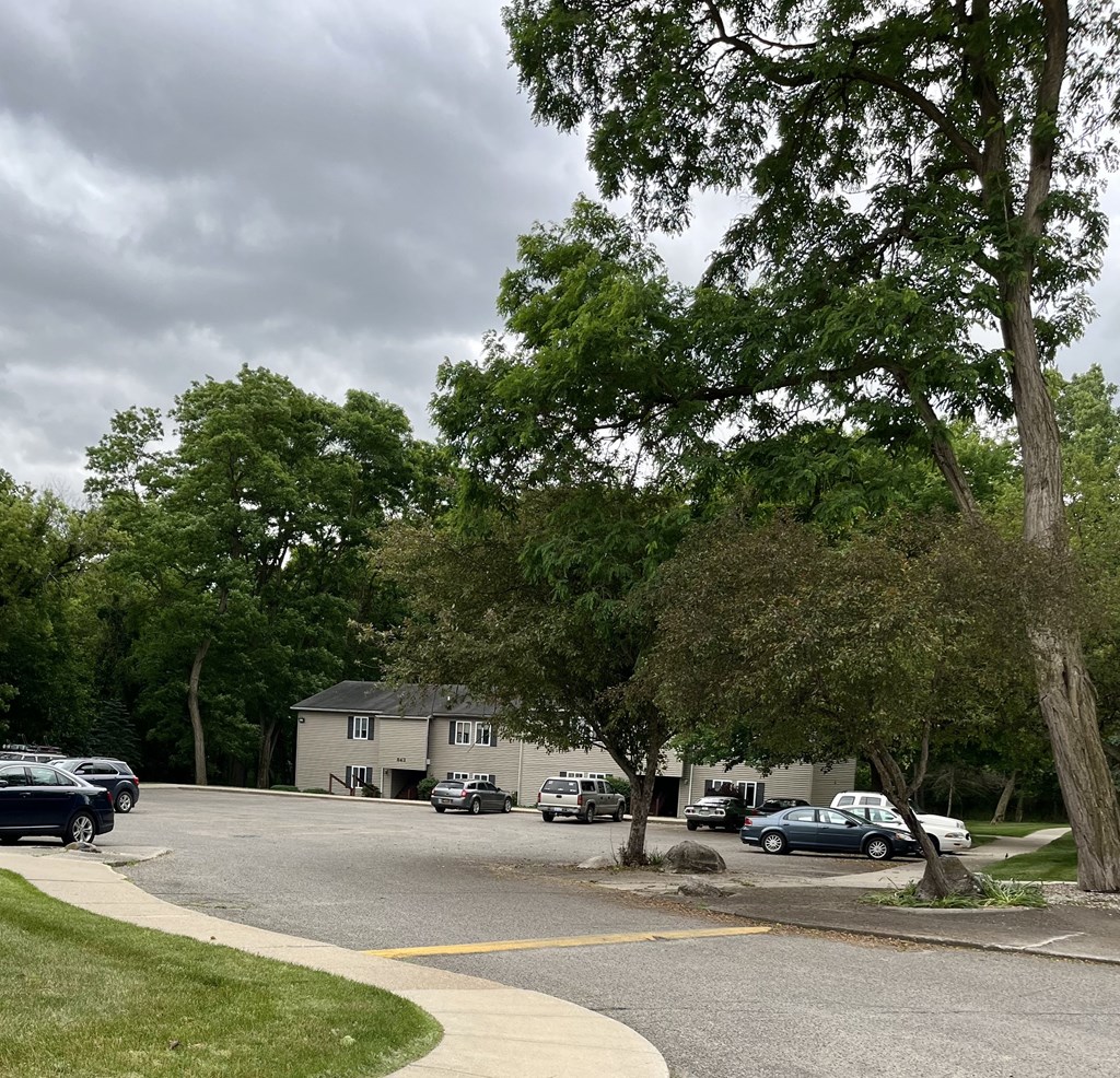 a parking lot with trees and cars in front of a house