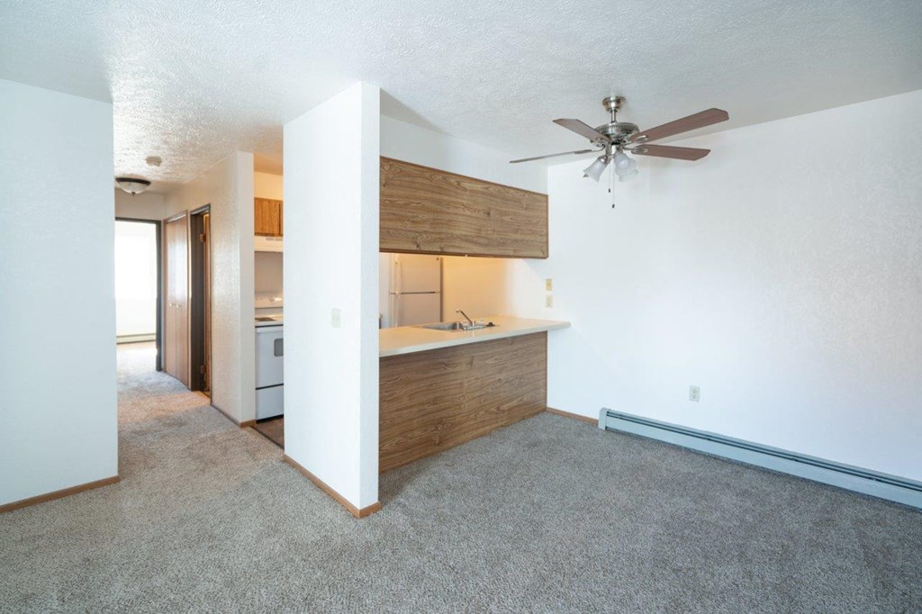 an empty living room with a ceiling fan and a kitchen