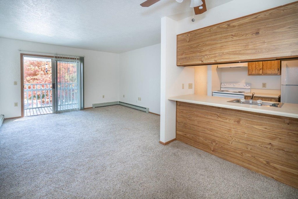 an empty living room with a kitchen and a sliding glass door