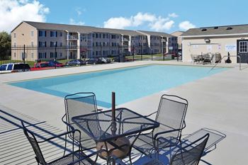 a swimming pool with tables and chairs next to an apartment building