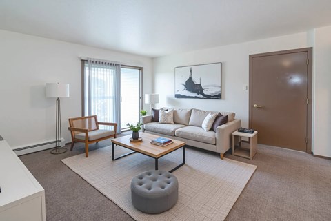 A living room with a couch, chair, ottoman, and a painting on the wall.
