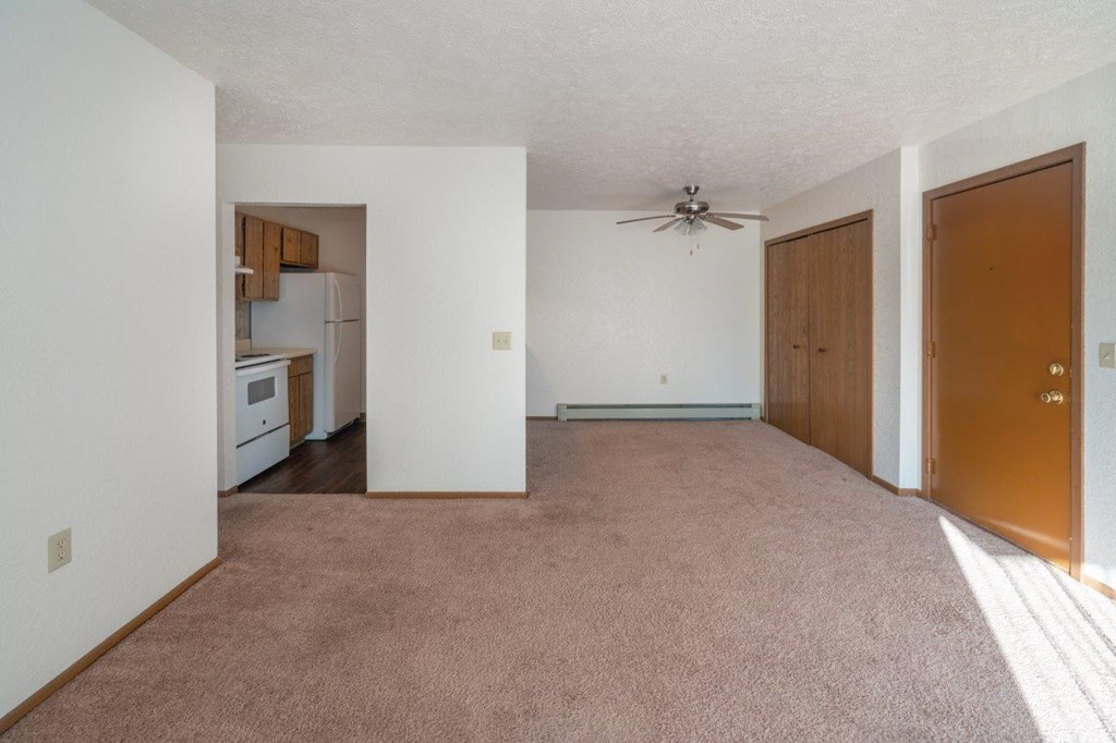 an empty living room with a ceiling fan and a kitchen