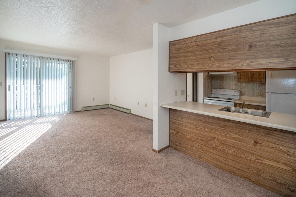 an empty living room with a kitchen and a window