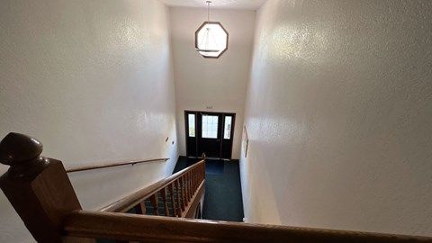 a view down the stairs of a hallway with a wooden railing and a black door