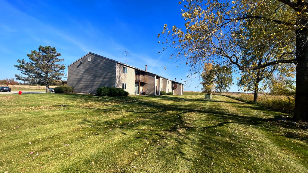 a barn with a green lawn and trees in front of it