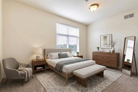 A bedroom with a bed, nightstand, chair, and mirror.