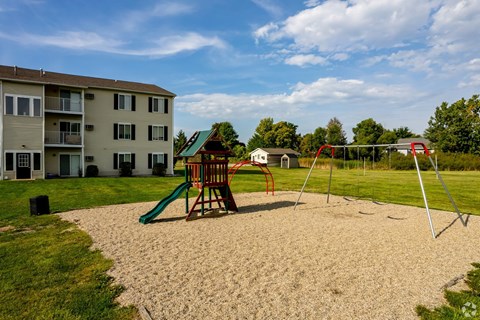 A playground with a green slide and a red swing set in front of a building.