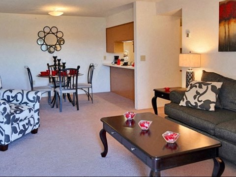 A living room with a grey couch, a coffee table, a dining table with chairs, and a painting on the wall.