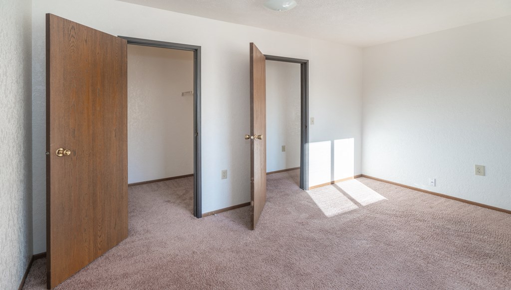 an empty bedroom with three doors and carpeting