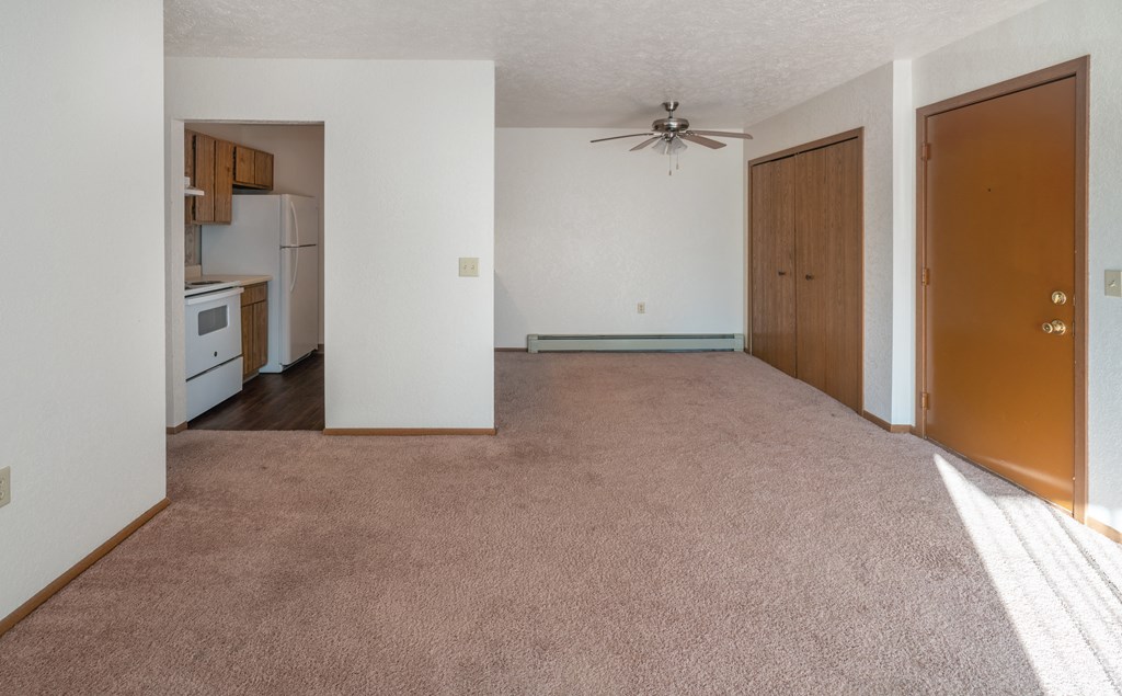 an empty living room with a ceiling fan and a kitchen