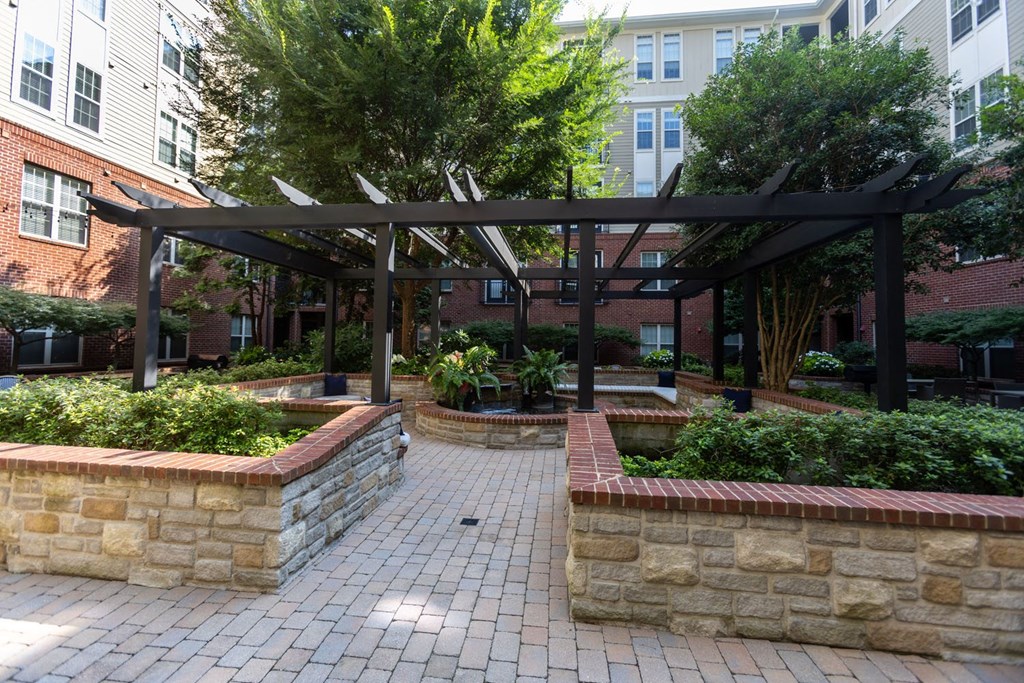 a courtyard with a pergola and a stone retaining wall with plants and trees