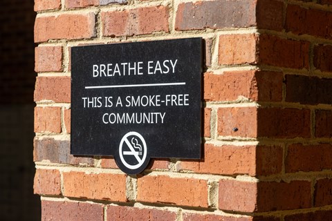 A sign on a brick wall that says "Breathe Easy, this is a smoke-free community.".