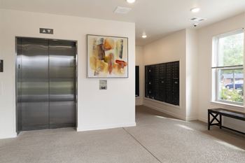 A hallway with a bench, a painting, and a wall of lockers.