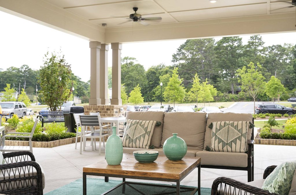 a covered patio with a couch table and chairs and a grill in the background