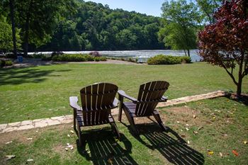 two wooden chairs sitting in the grass near the water