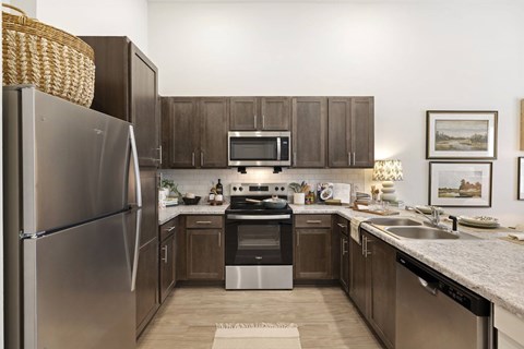 A kitchen with a refrigerator, microwave, oven, sink, and cabinets.