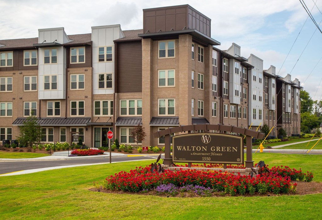an apartment building with a sign in front of a lawn and flowers