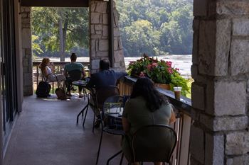 people sitting at tables on a porch overlooking the river