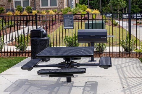 A black picnic table with a trash can and a recycling bin in front of a black fence.