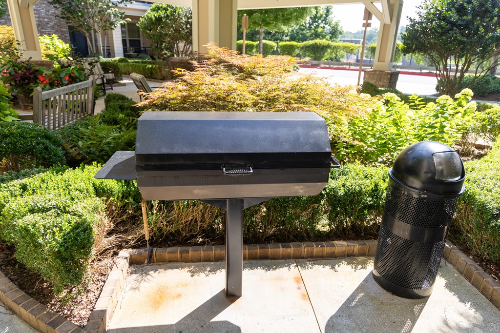 a charcoal grill and a trash can sit in front of a garden