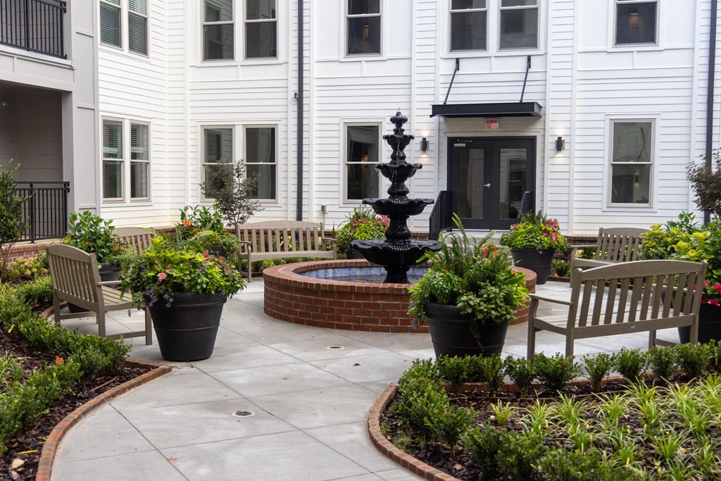 a courtyard with a fountain and benches in front of a white building