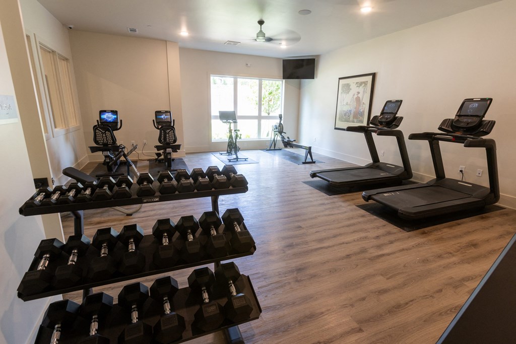 a spacious fitness room with cardio equipment and a large window
