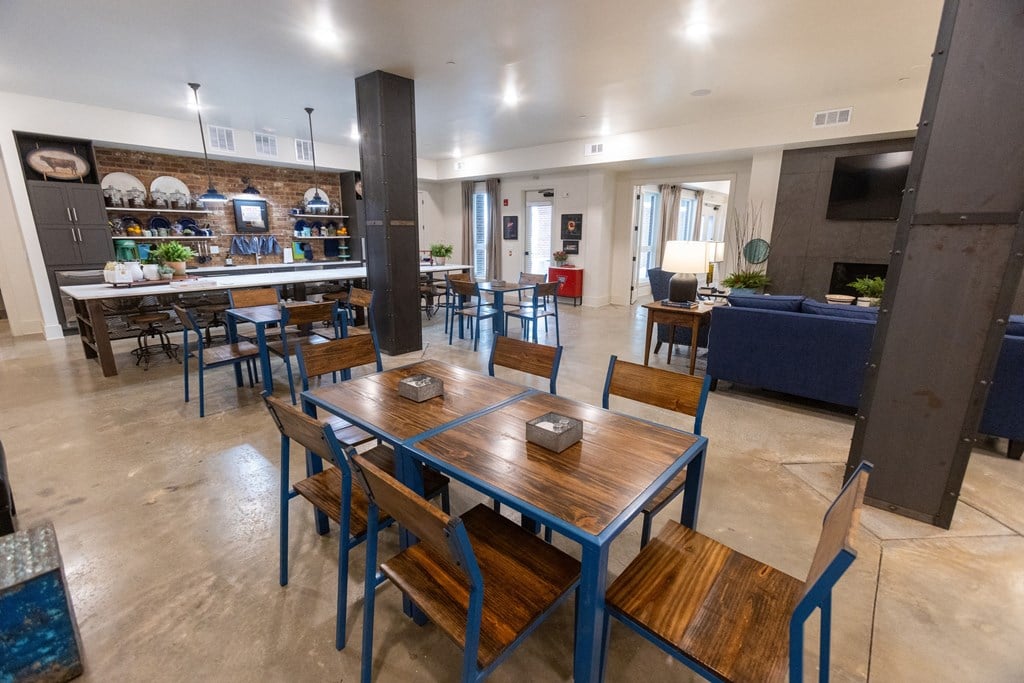 a dining area with wooden tables and chairs and a kitchen in the background