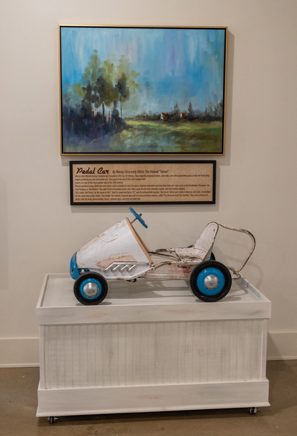 a childs pedal car with blue wheels sits on a white pedestal in front of a