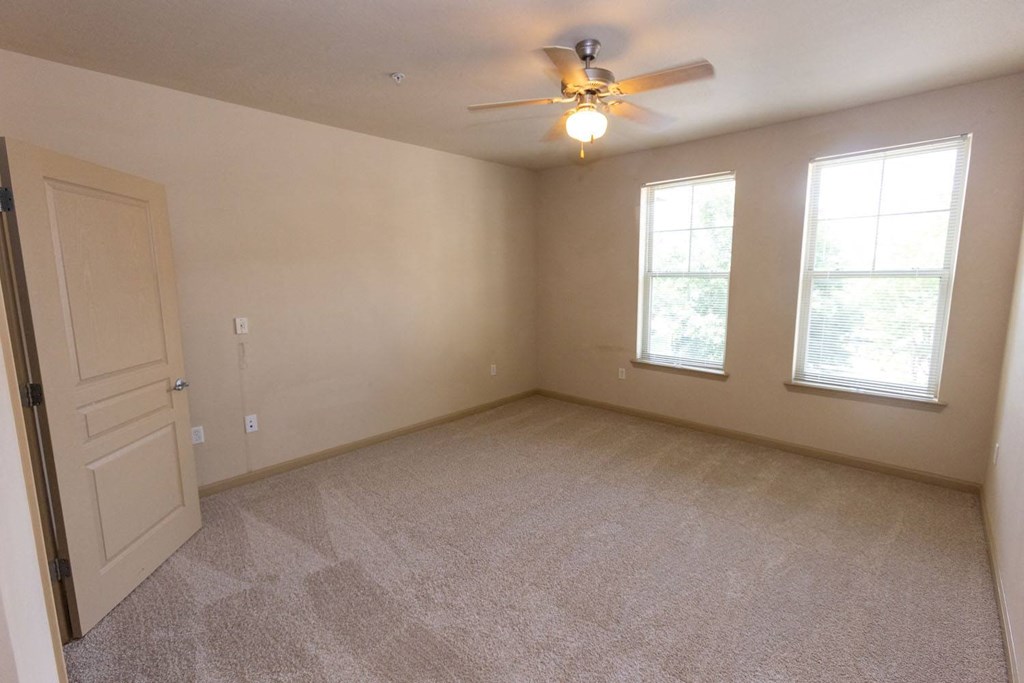 an empty room with a ceiling fan and three windows