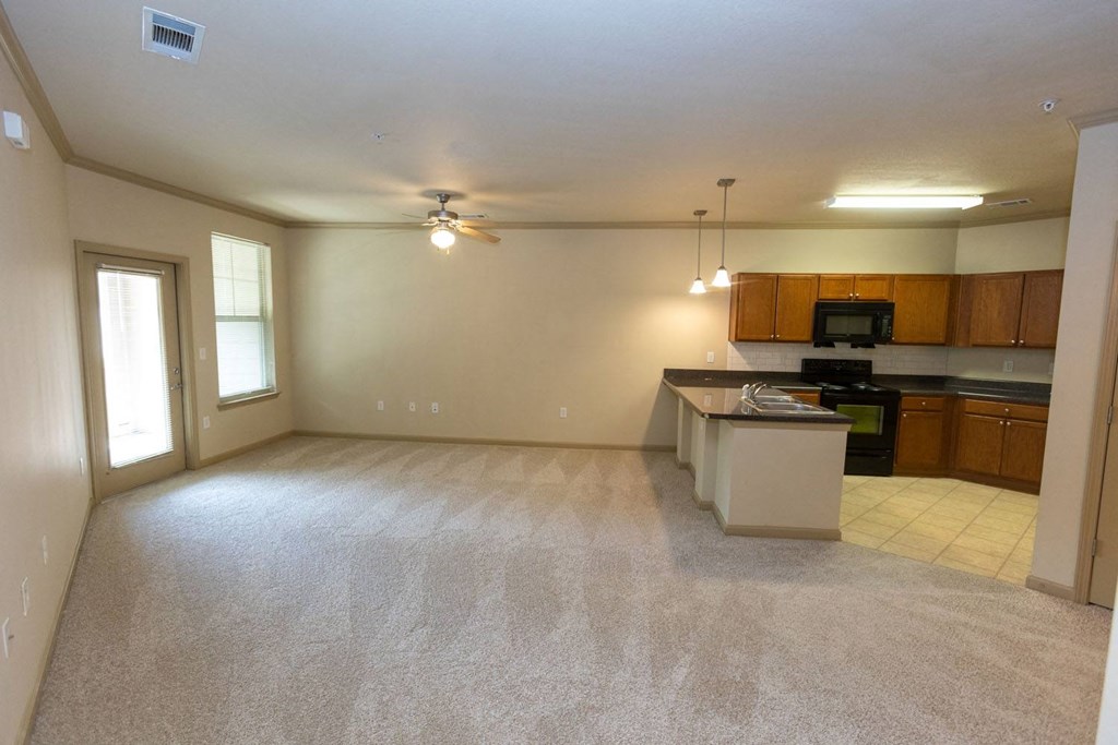 an empty living room with a kitchen in the background