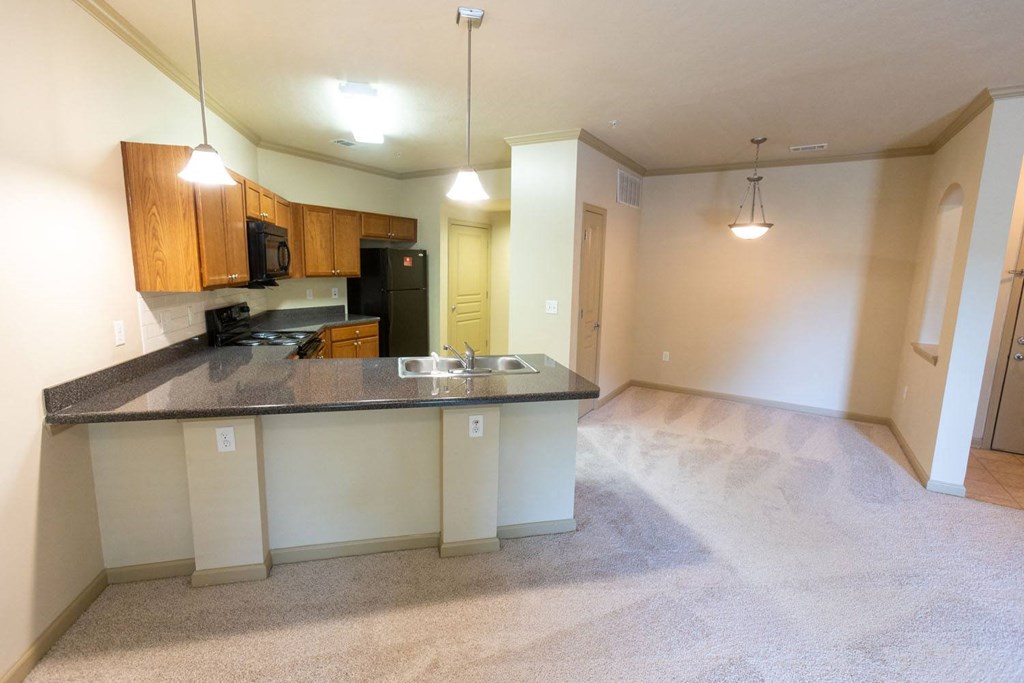an empty living room with a kitchen in the background