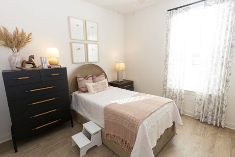 A bedroom with a bed, nightstand, and a dresser with a vase on top.