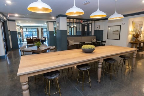 A long wooden table with four stools is in the center of a room with a large window.