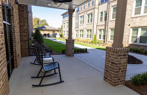 A view of a porch with rocking chairs and a building in the background.