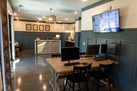 A room with a desk, chairs, and a TV mounted on the wall.