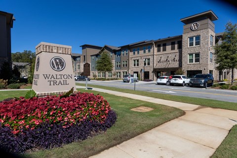 A Walton Trail sign is in front of a building with a flower bed.