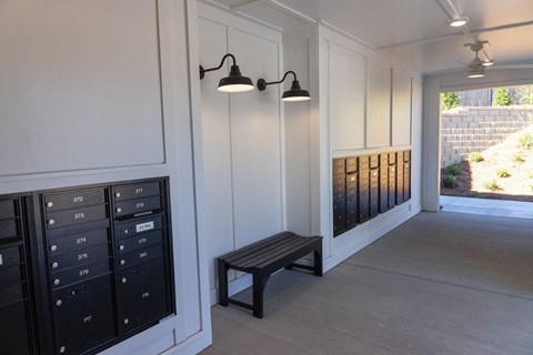 A bench is placed under a light fixture in a room with mailboxes on the wall.
