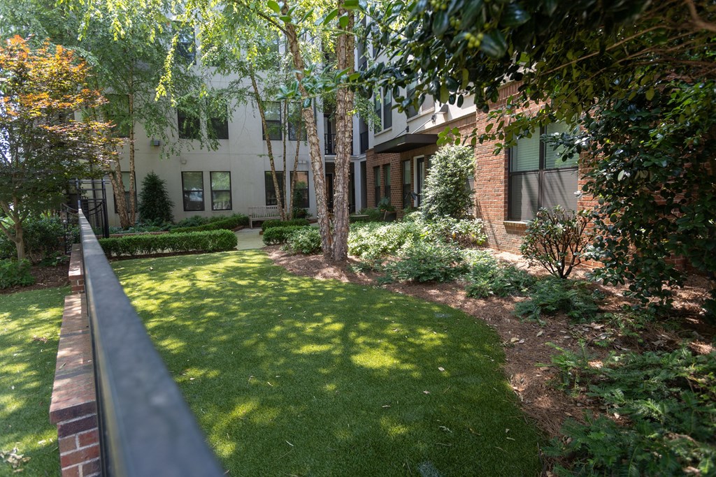 a grassy area with trees and bushes in front of a building