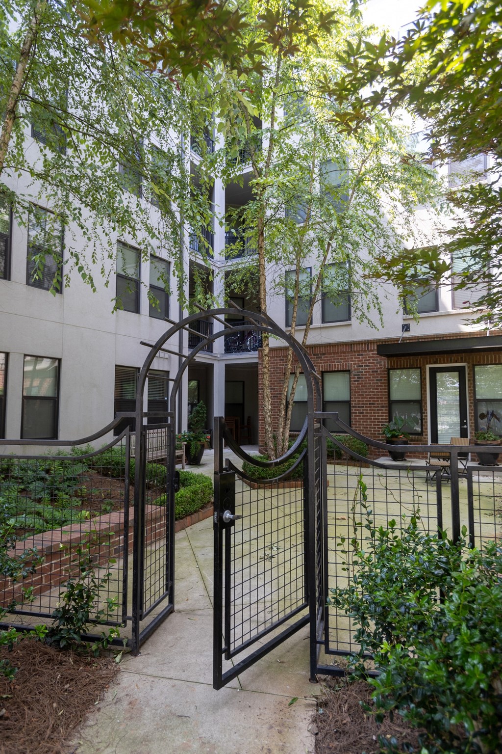 an open gate leads to a brick building with trees in the background