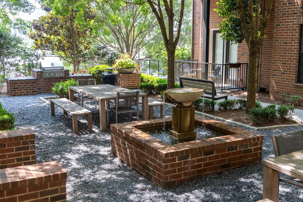 a seating area with a fountain and benches in front of a brick building