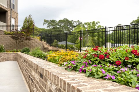 A brick wall with a black fence and flowers in front.