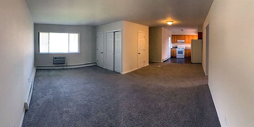 an empty living room with a kitchen in the background