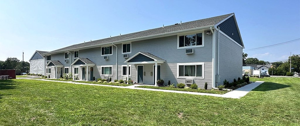 a large gray house with a gray roof and green grass in front of it at Brookwood at Sayville, Sayville