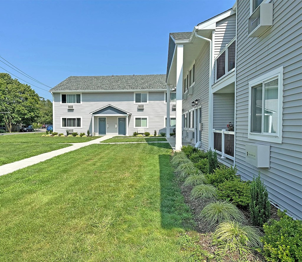 a view of the exterior of a gray building with a blue garage door and a green lawn at Brookwood at Sayville, Sayville, NY