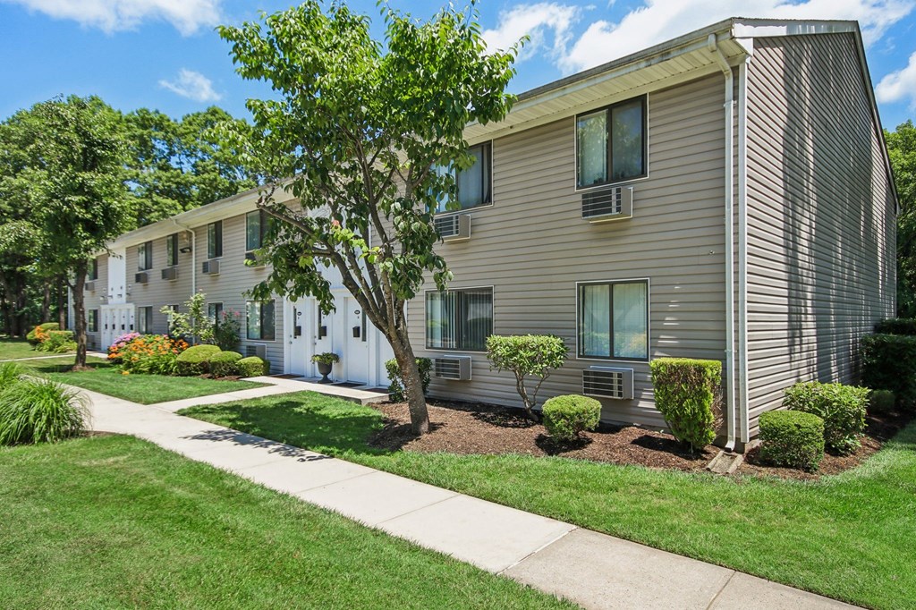 Outside view of apartment with a sidewalk and trees in front at Brookwood at Ridge, New York, 11961
