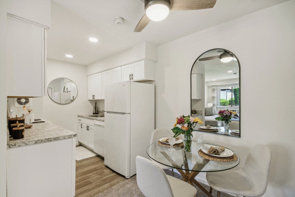 a white kitchen with granite counter top and dining area with a glass table and chairs at Brookwood at Ridge, New York, 11961