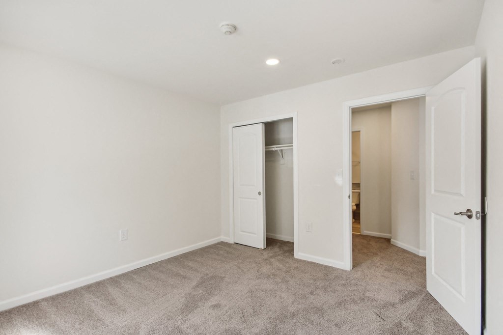 a bedroom with white walls and a door to a closet at Brookwood at Ridge, New York, 11961