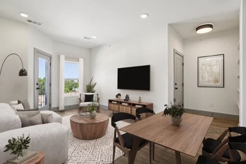 A modern living room with a wooden table and chairs, a couch, and a flat-screen TV mounted on the wall.
