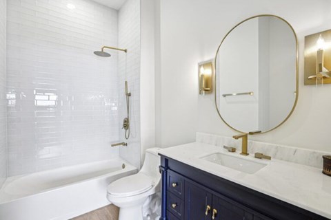 A white bathroom with a round mirror and a gold faucet.